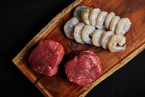 A cutting board displaying a shrimp and steak bundle, ready for preparation.