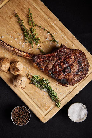 A grilled USDA Platinum Tomahawk Ribeye steak displayed on a cutting board, accented with herbs and spices for flavor.