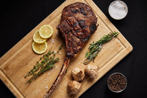 A grilled USDA Platinum Tomahawk Ribeye steak displayed on a cutting board, accented with garlic, lemon and spices for flavor.