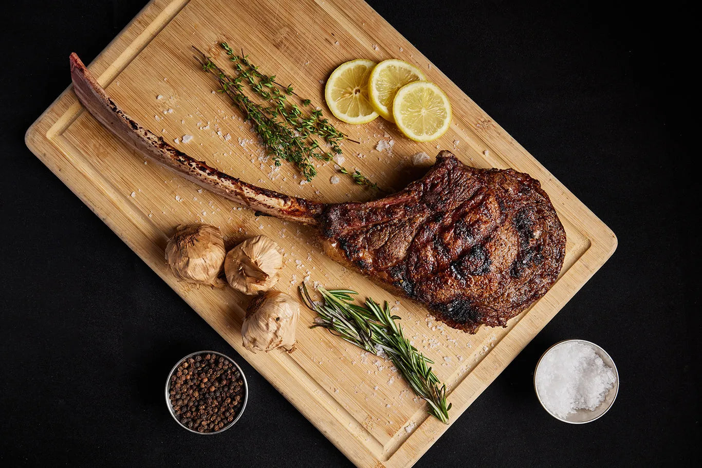 A grilled USDA Platinum Tomahawk Ribeye steak displayed on a cutting board, accented with herbs, garlic and spices for flavor.