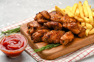 A wooden cutting board featuring grilled chicken wings, fries, and a side of ketchup for dipping.