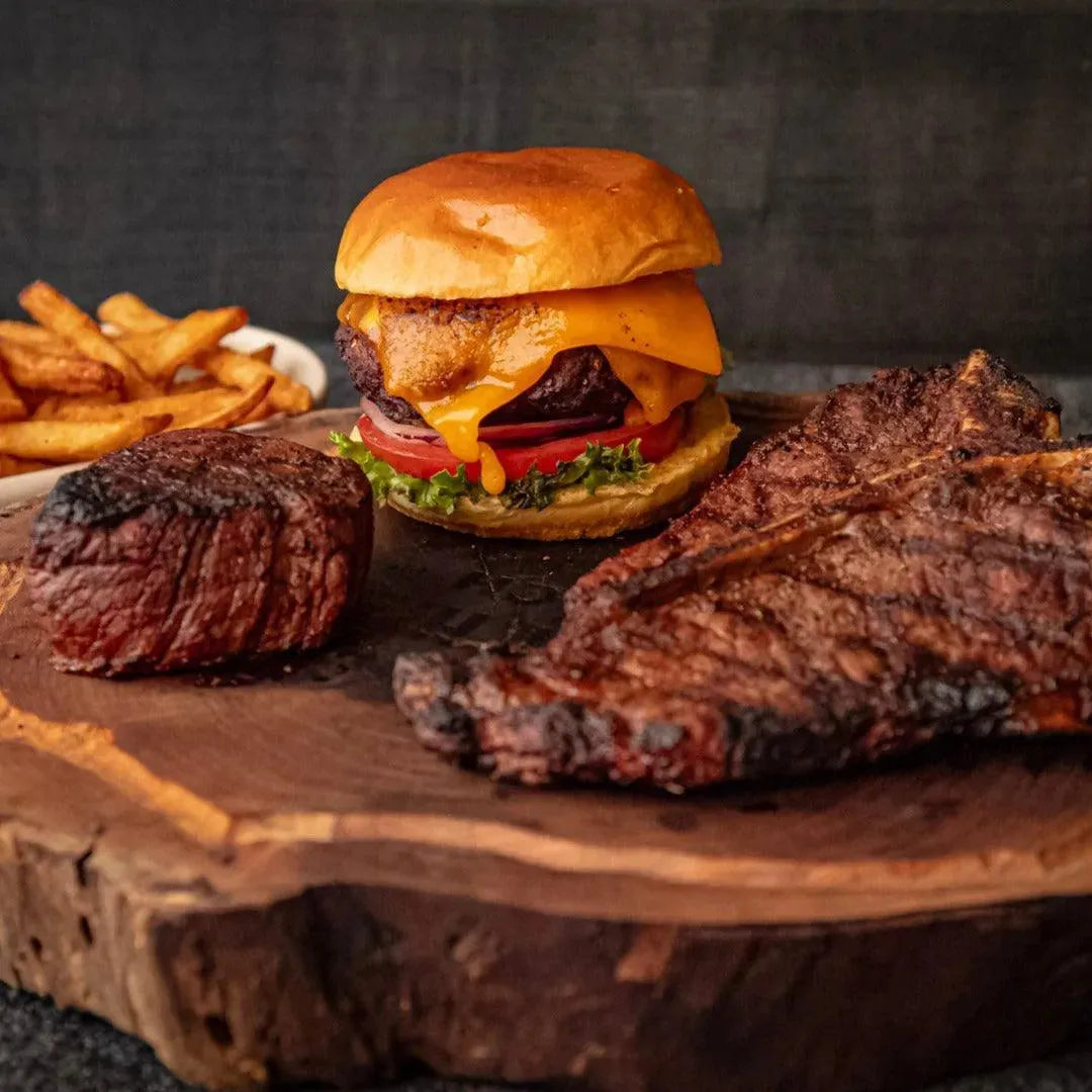 A T-Bone steak, Filet Mignon and a burger displayed on a wooden board, showcasing a meat bundle.