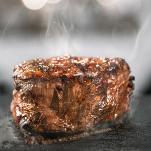 A sizzling steak being cooked on a black plate, showcasing a Filet Mignon Center Cut USDA Choice.