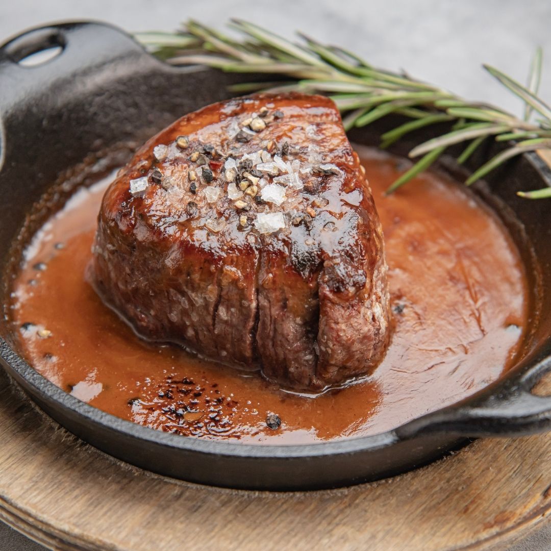 A filet mignon steak sizzling in a skillet with rich gravy and fresh rosemary.