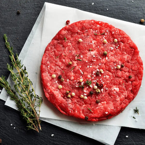 A raw Black Angus beef burger patty prepared with spices displayed on a dark background